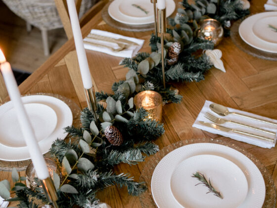 Parquet dning table set with a Christmas runner going down the middle, white taper candles and white crockery.