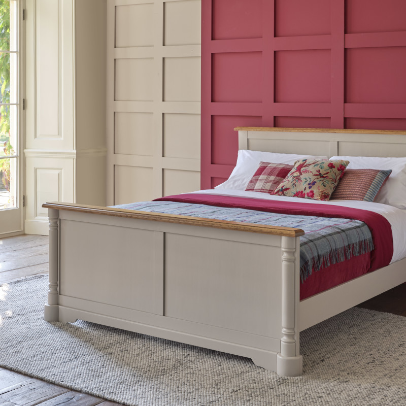 Cream painted double bed in a cream and pink bedroom, against a panelled wall. 