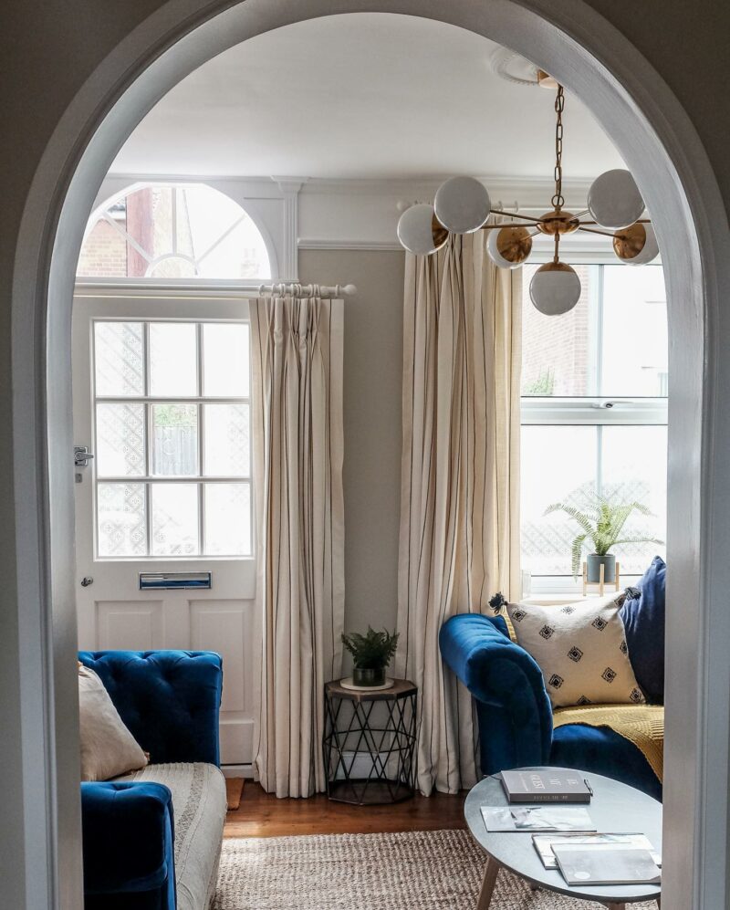 Two sofas-living room furniture-blue velvet sofas-chesterfield sofas-archway-neutral living room-draped curtains-statement ceiling lamp-metal side table-jute rug