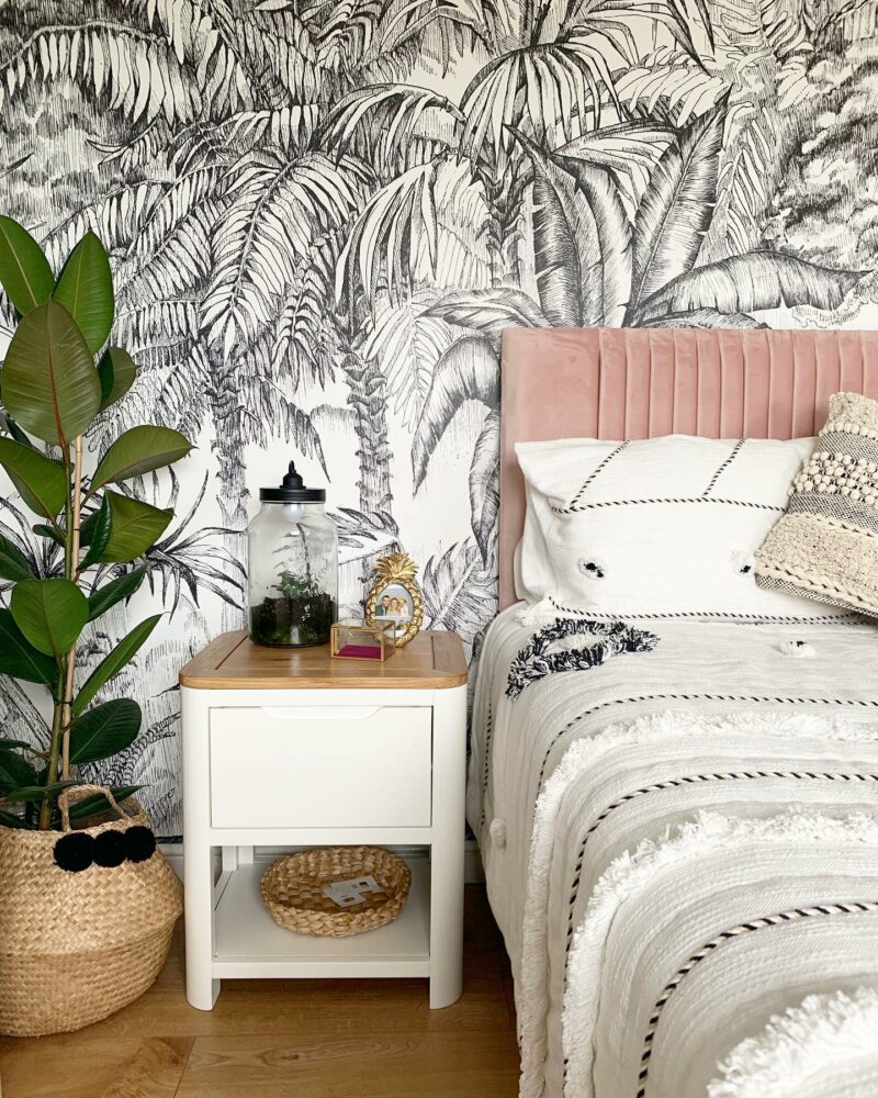 Oak Furnitureland white and oak Romsey bedside table with monochrome wallpaper, pink upholstered bed and plants.