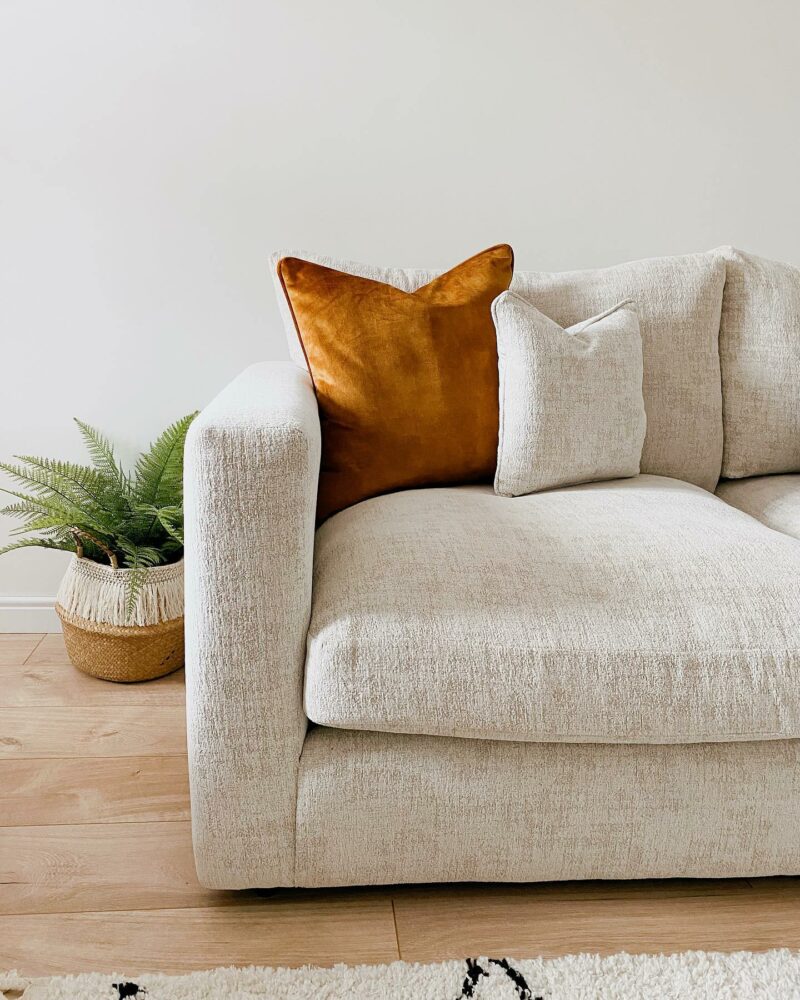 Cream Oak Furnitureland sofa close up of the corner featuring a mustard scatter cushion and a houseplant in the background.